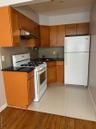 Kitchen with brown cabinetry, range, fridge, exhaust hood, and dark stone counters