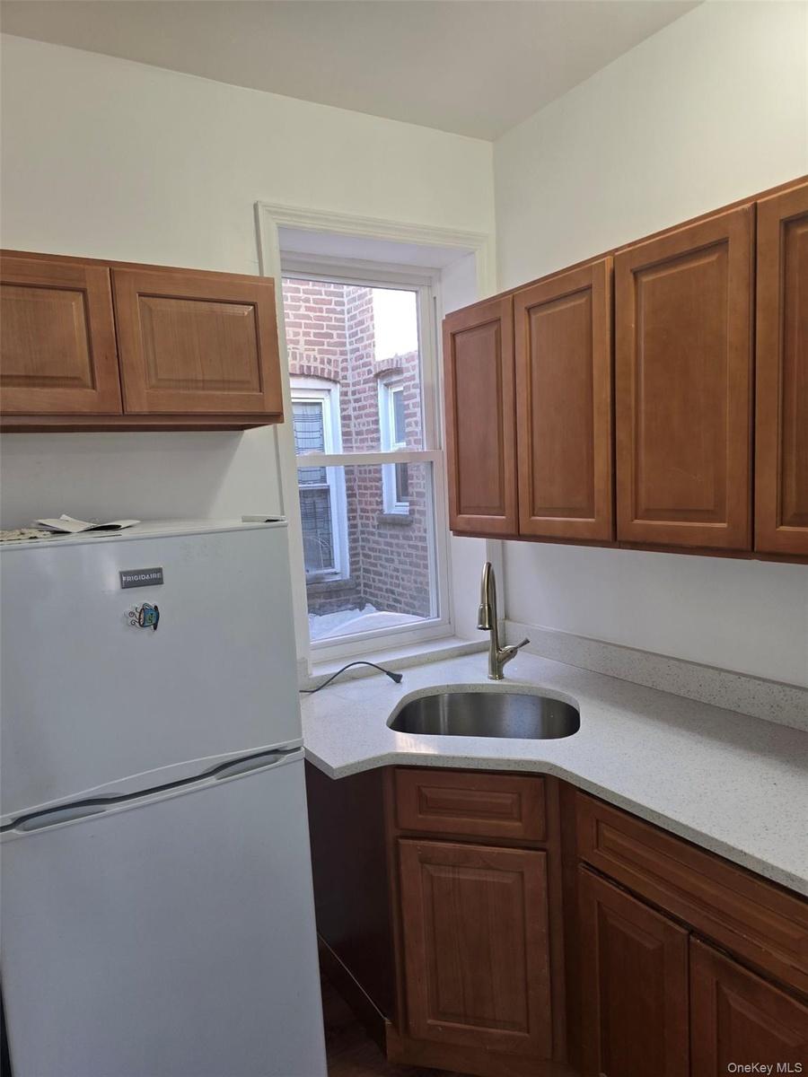 Kitchen with freestanding refrigerator, brown cabinetry, and light stone countertops