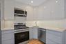 Kitchen with appliances with stainless steel finishes, gray cabinetry, light stone counters, and decorative backsplash