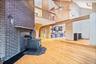 Unfurnished living room with a wood stove, brick wall, wood-type flooring, a high ceiling, and ceiling fan