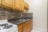 Kitchen with white gas range oven, dark countertops, decorative backsplash, light tile patterned flooring, and light brown cabinetry