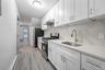 Kitchen with stainless steel appliances, a baseboard heating unit, white cabinetry, under cabinet range hood, and light stone counters