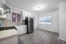 Kitchen with light stone counters, freestanding refrigerator, white cabinets, range hood, and decorative backsplash