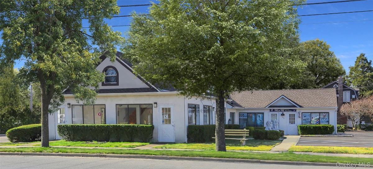 View of front of house with stucco siding, a shingled roof, uncovered parking, and a front lawn