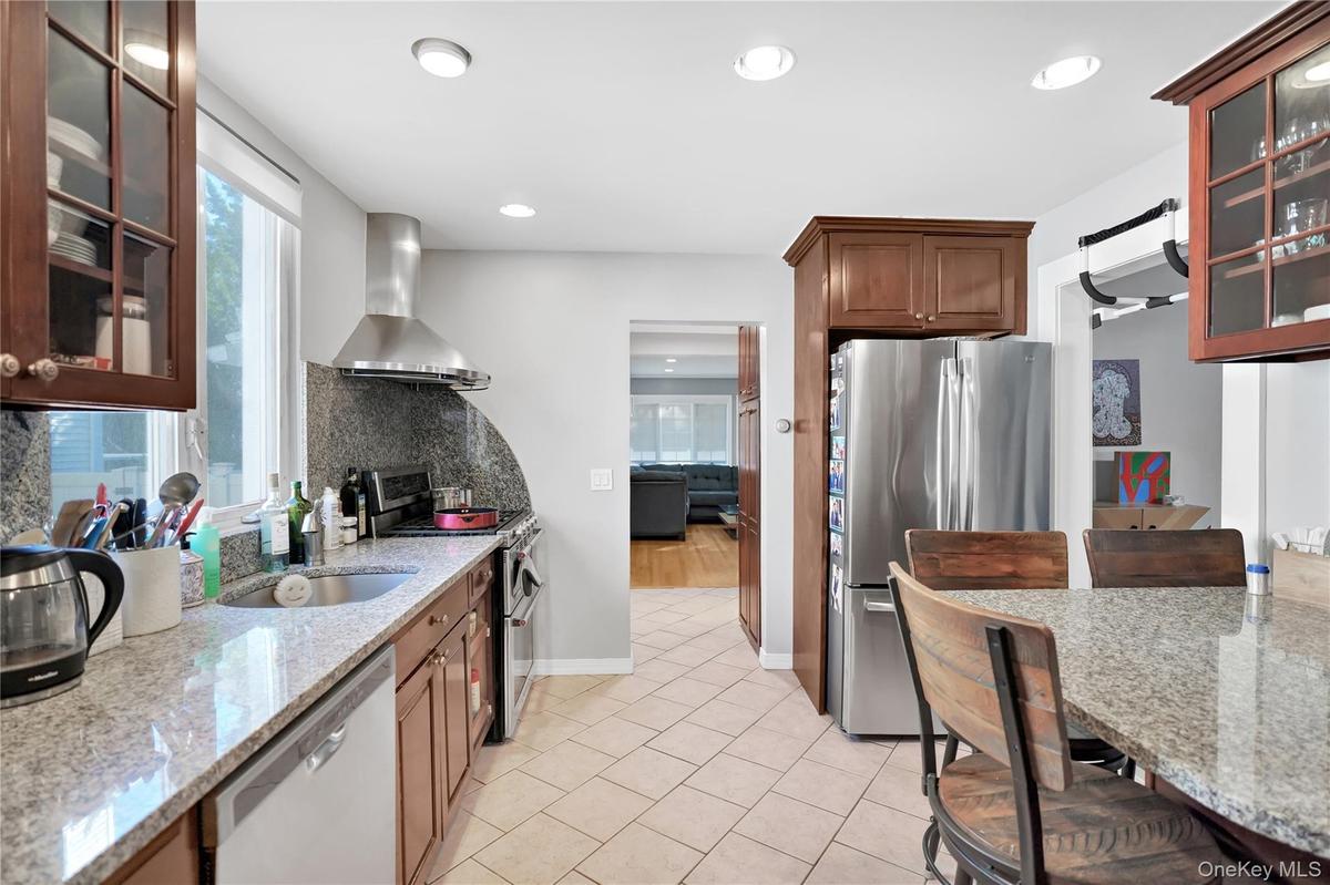 Kitchen with glass insert cabinets, stainless steel appliances, light stone countertops, wall chimney exhaust hood, and a breakfast bar area