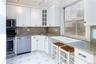 Kitchen featuring stainless steel appliances, white cabinets, light stone counters, and glass insert cabinets