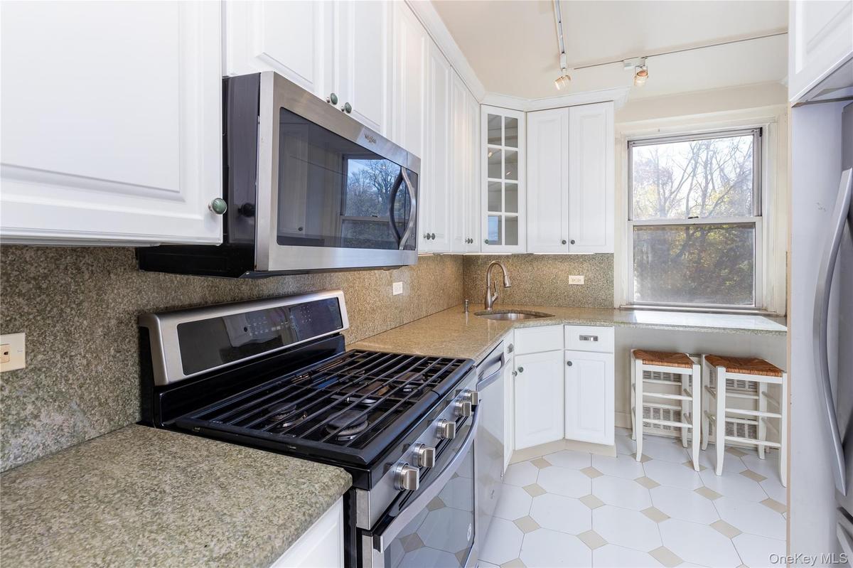 Kitchen featuring stainless steel appliances, white cabinets, decorative backsplash, light stone counters, and glass insert cabinets