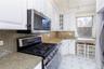 Kitchen featuring stainless steel appliances, white cabinets, decorative backsplash, light stone counters, and glass insert cabinets