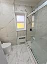 Full bath featuring light marble finish flooring, a marble finish shower, radiator, and tile walls