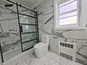 Full bathroom featuring light marble finish floors, tile walls, a marble finish shower, heating unit, and radiator