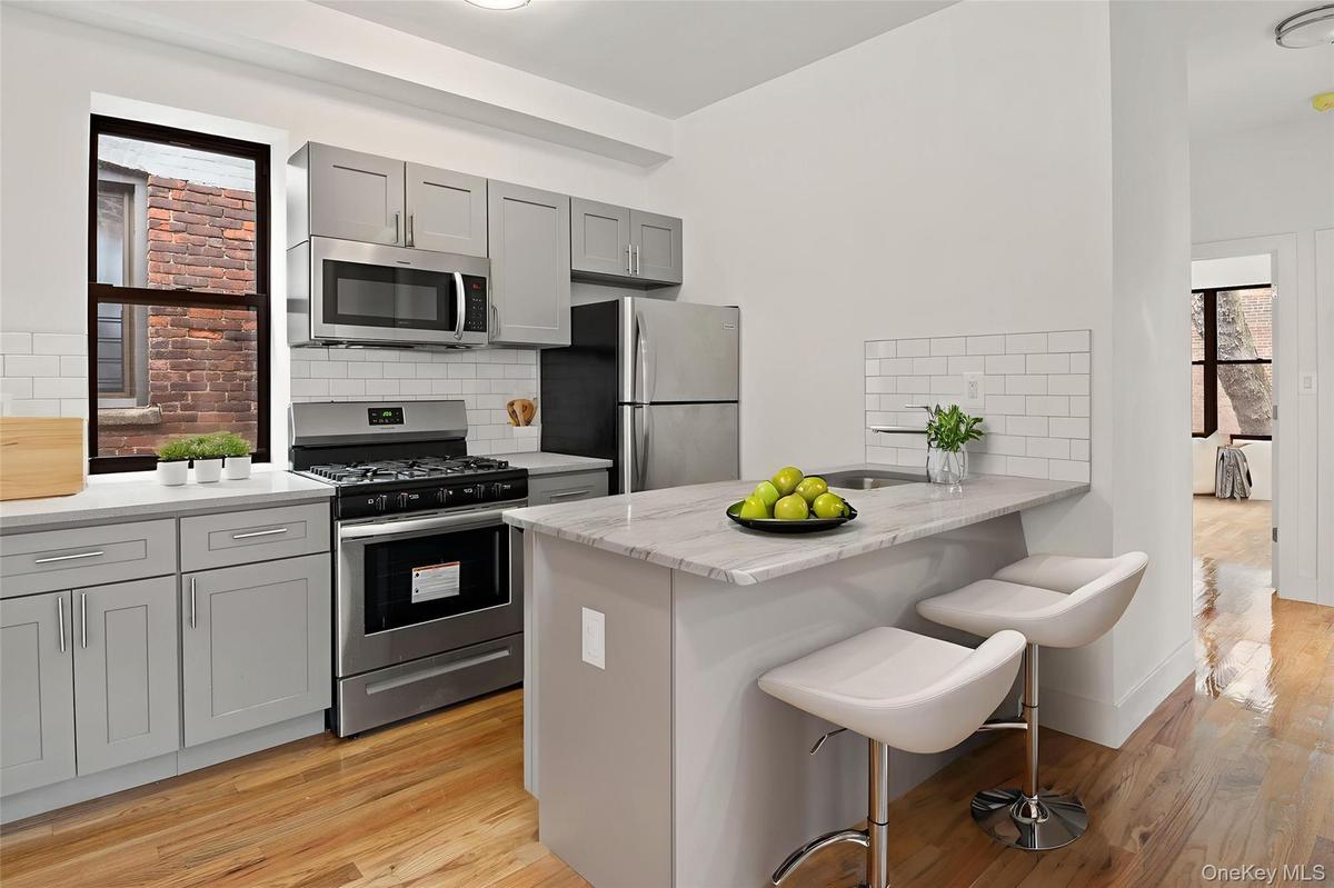 Kitchen featuring gray cabinets, appliances with stainless steel finishes, a kitchen bar, tasteful backsplash, and light stone counters