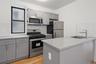 Kitchen with gray cabinets, appliances with stainless steel finishes, decorative backsplash, light stone countertops, and light wood-style flooring