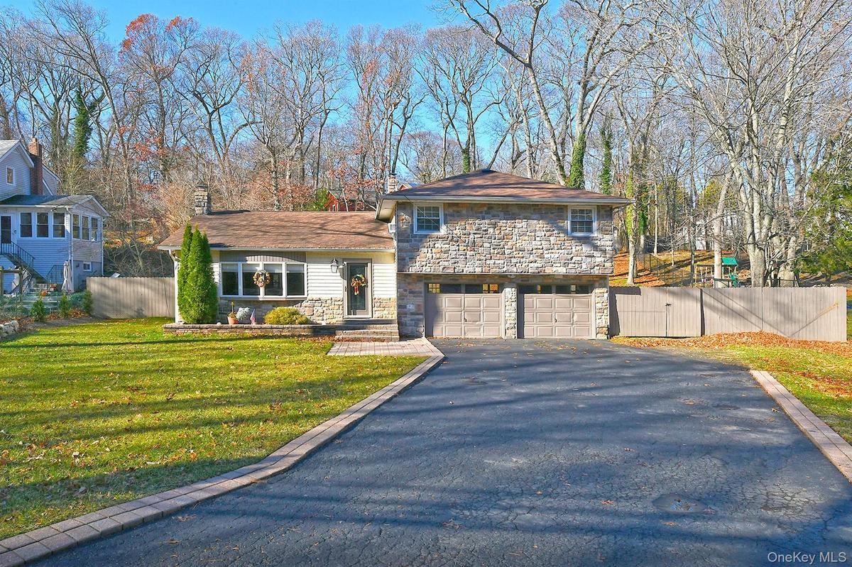 Split level home with stone siding, asphalt driveway, a garage, and a gate