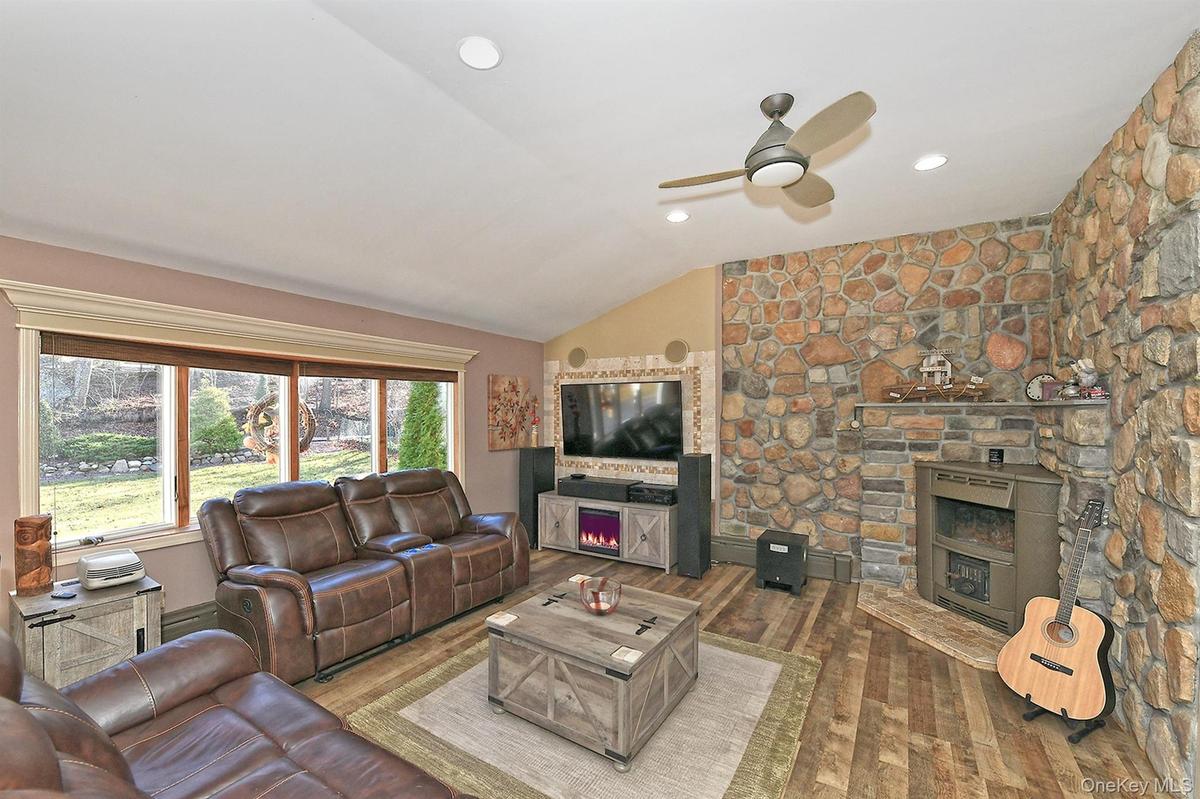 Living area with vaulted ceiling, a warm lit fireplace, hardwood / wood-style floors, a ceiling fan, and recessed lighting