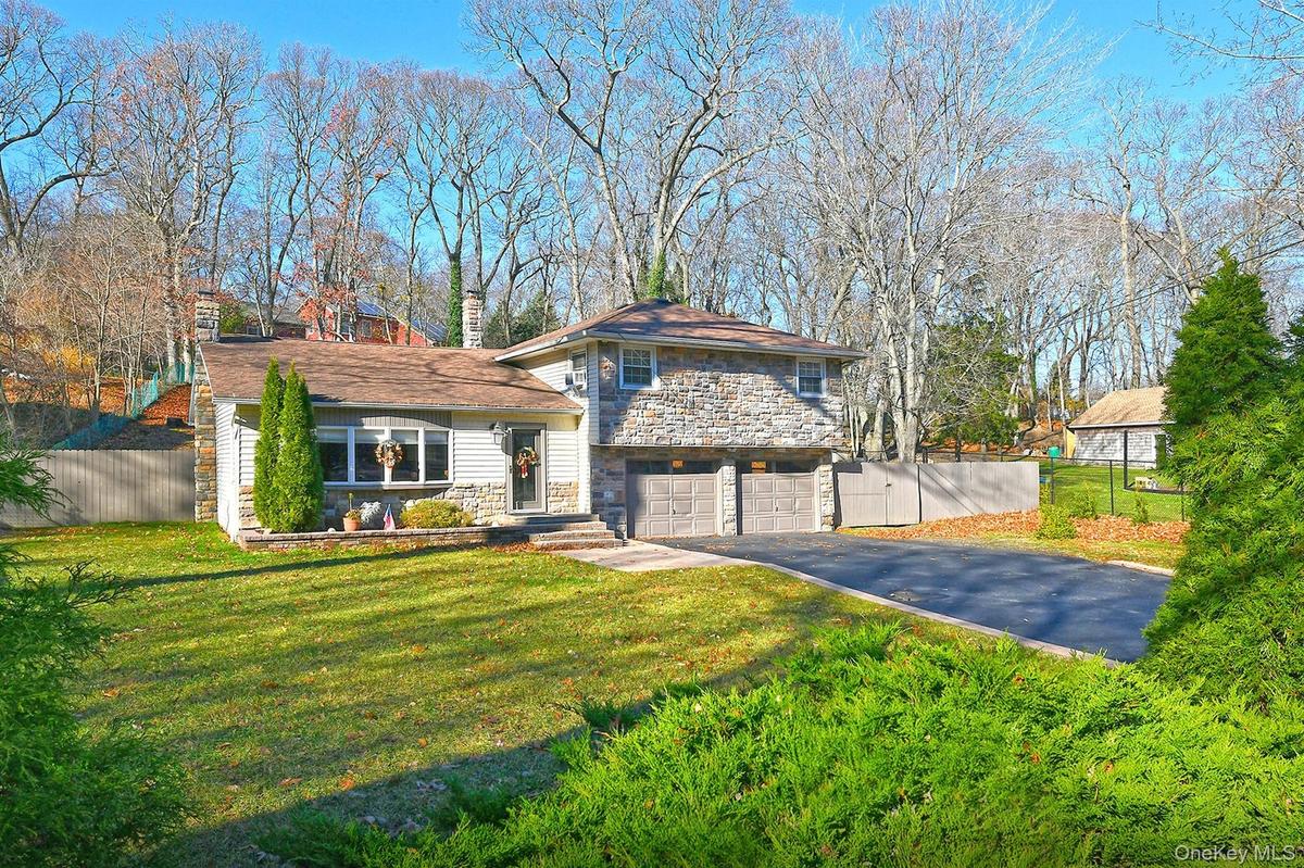 Split level home with stone siding, asphalt driveway, a chimney, and an attached garage