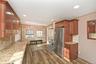 Kitchen with freestanding refrigerator, backsplash, brown cabinets, light stone countertops, and dark wood-style floors