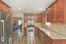 Kitchen with appliances with stainless steel finishes, light stone counters, dark wood-type flooring, brown cabinets, and under cabinet range hood