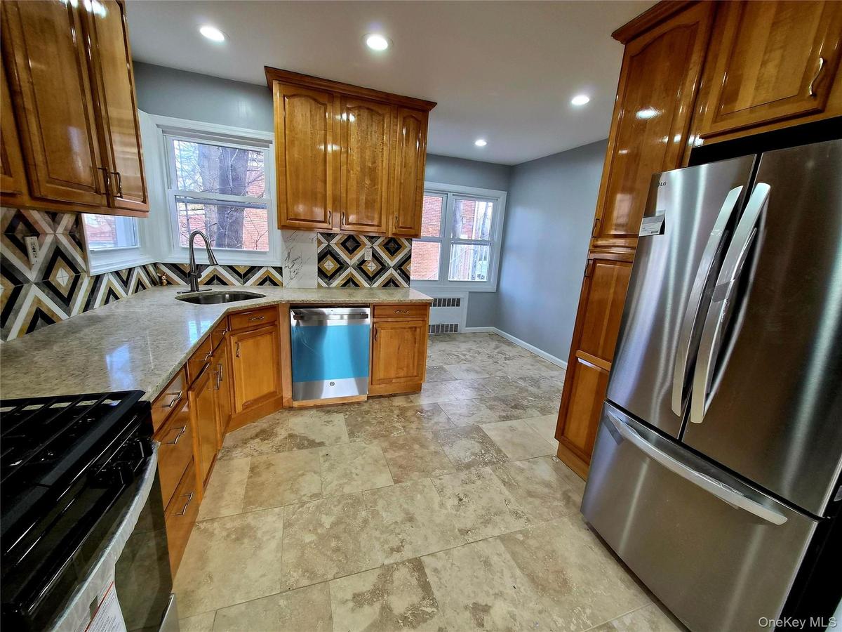Kitchen featuring stainless steel appliances, brown cabinets, light stone counters, recessed lighting, and tasteful backsplash