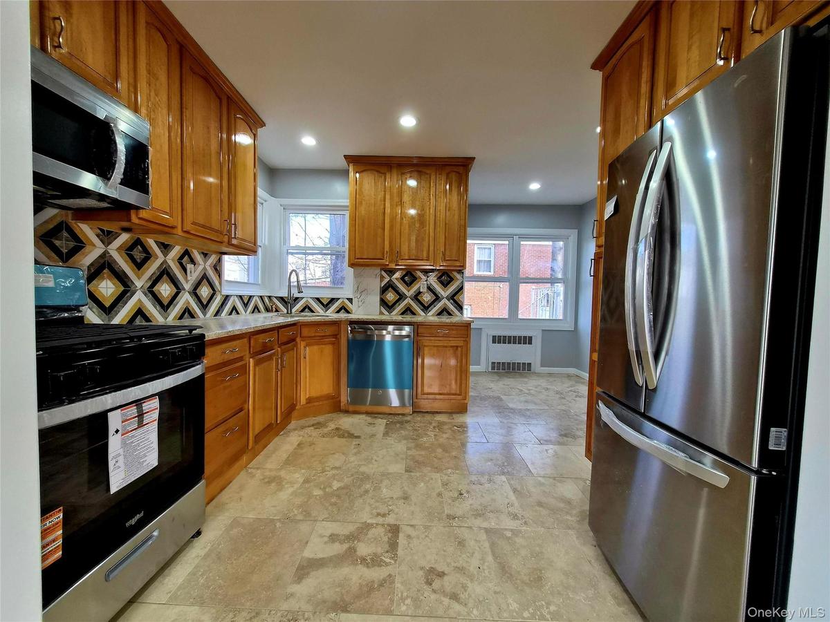 Kitchen featuring appliances with stainless steel finishes, brown cabinets, decorative backsplash, radiator heating unit, and recessed lighting