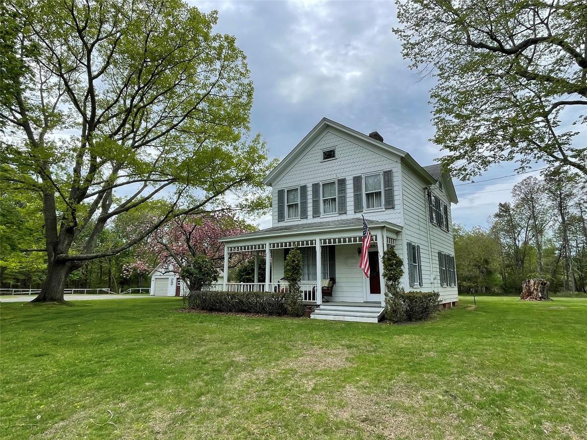 Victorian-style house featuring covered porch, a front yard, an outbuilding, and a chimney
