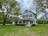 Victorian-style house featuring covered porch, a front yard, an outbuilding, and a chimney