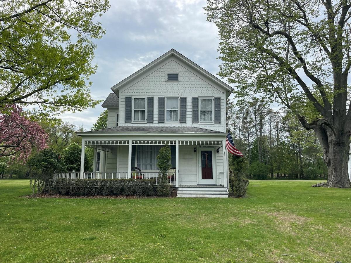 Victorian-style house with covered porch, a front lawn, and roof with shingles