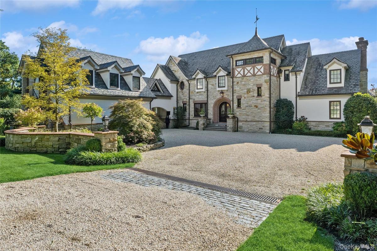 View of front facade featuring a high end roof, curved driveway, stucco siding, stone siding, and a chimney