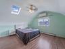 Bedroom featuring a skylight, lofted ceiling, a baseboard radiator, wood finished floors, and a wall mounted air conditioner