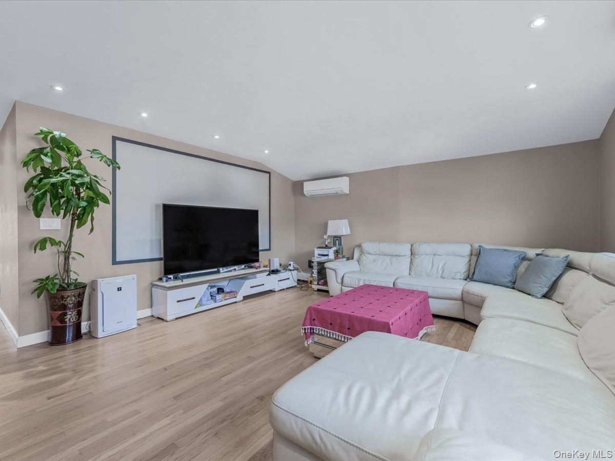 Living area featuring light wood-type flooring, recessed lighting, a wall mounted air conditioner, and vaulted ceiling