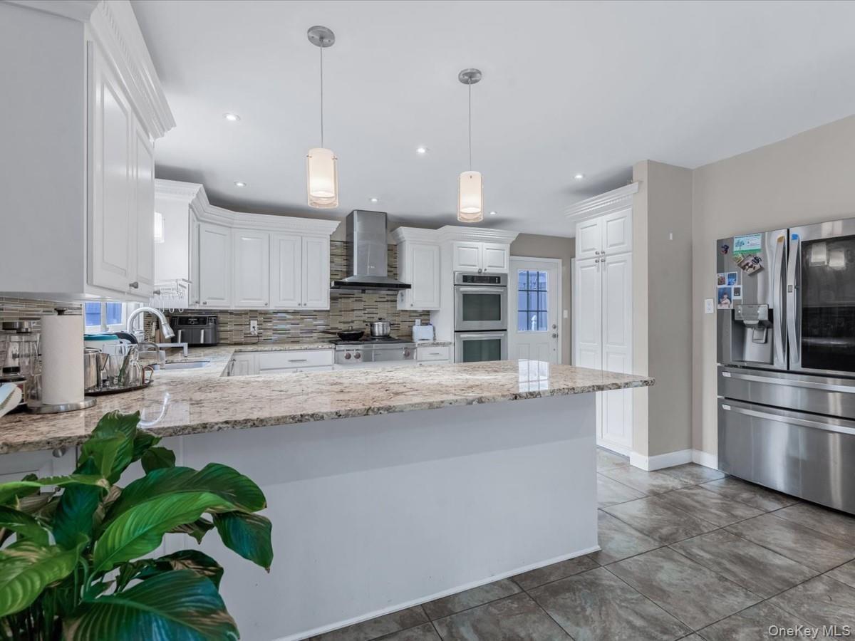 Kitchen with stainless steel appliances, white cabinets, a peninsula, light stone countertops, and wall chimney range hood