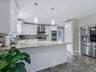 Kitchen with stainless steel appliances, white cabinets, a peninsula, light stone countertops, and wall chimney range hood