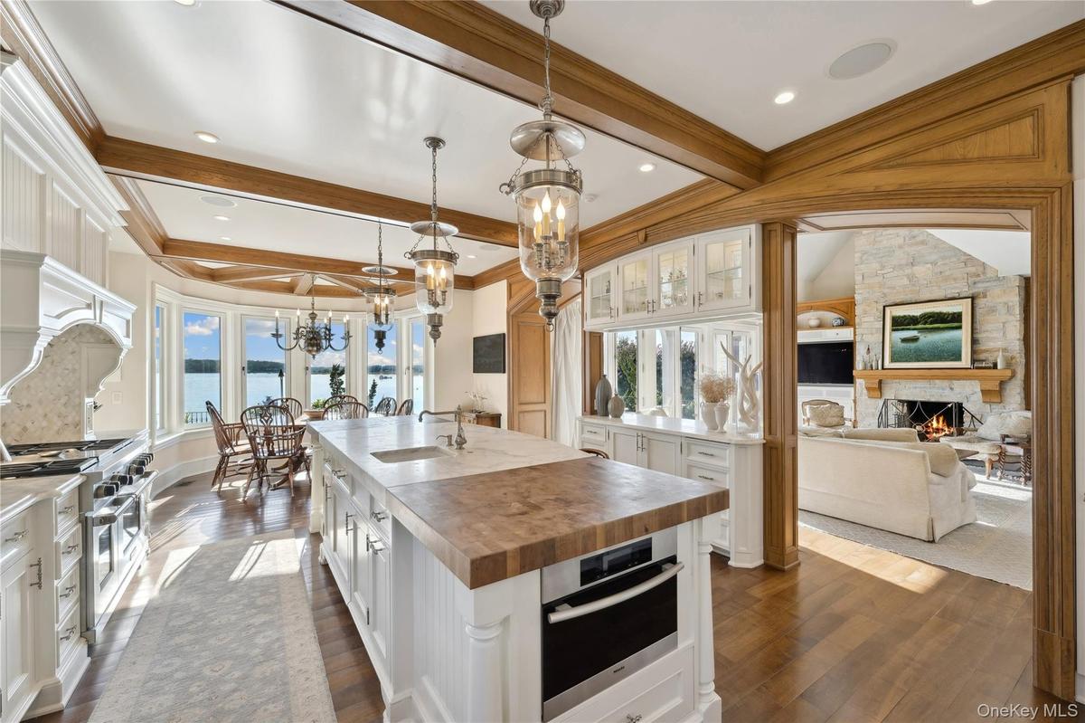 Kitchen featuring butcher block counters, decorative light fixtures, a kitchen island with sink, white cabinetry, and appliances with stainless steel 