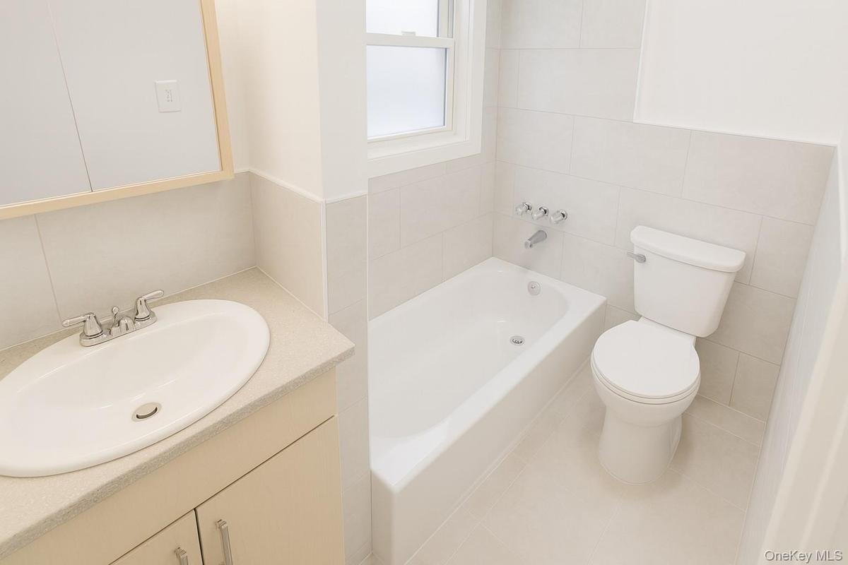Full bathroom featuring a bath, vanity, tile walls, and tile patterned flooring
