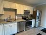 Kitchen featuring white cabinets, stainless steel appliances, light stone countertops, under cabinet range hood, and light wood finished floors