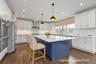 Kitchen featuring blue cabinetry, hanging light fixtures, white cabinets, a kitchen island, and light stone counters
