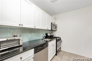 Kitchen with dark countertops, white cabinetry, appliances with stainless steel finishes, light tile patterned flooring, and backsplash