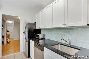 Kitchen featuring white cabinets, tasteful backsplash, stainless steel appliances, light tile patterned floors, and dark stone countertops