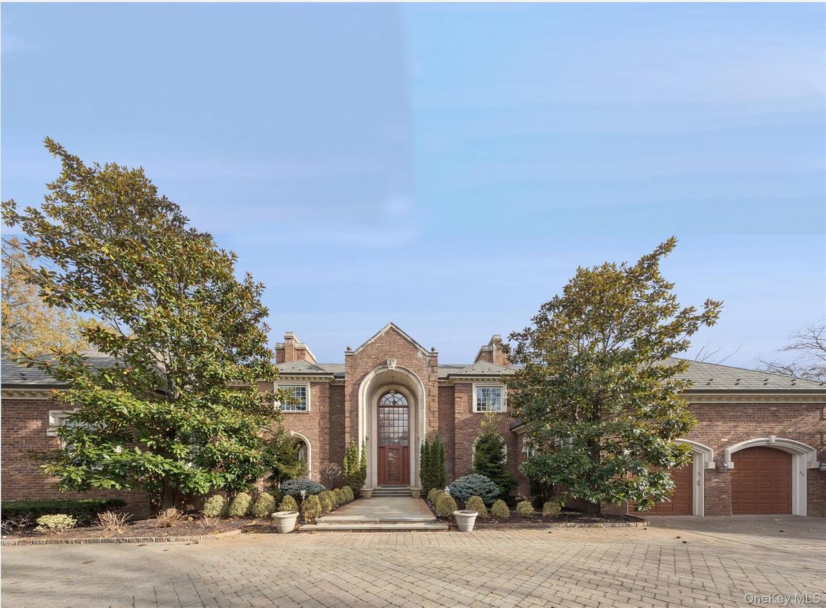 View of front of home with brick siding, driveway, a chimney, and a garage