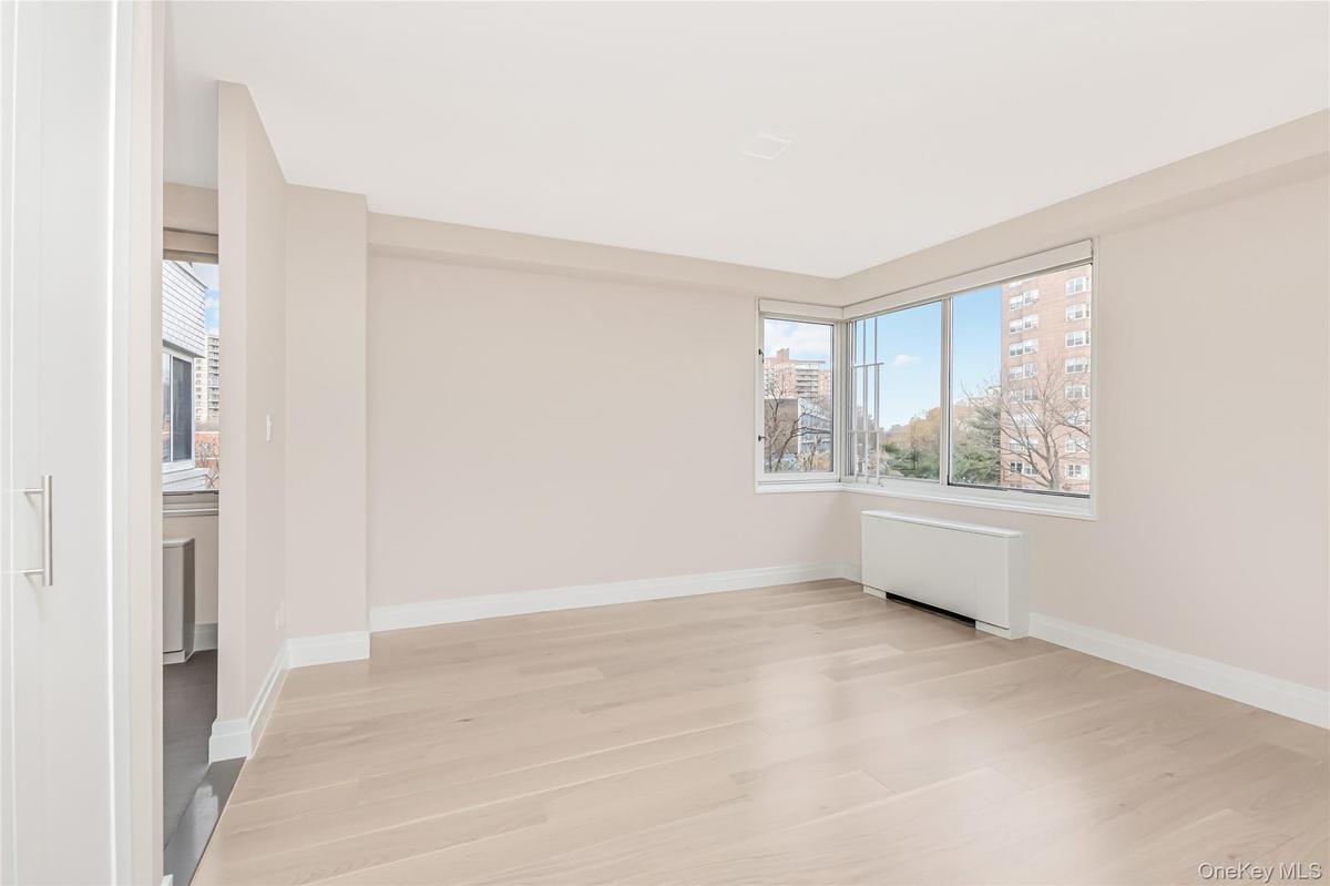 Unfurnished room with radiator, plenty of natural light, light wood-style flooring, and a city view