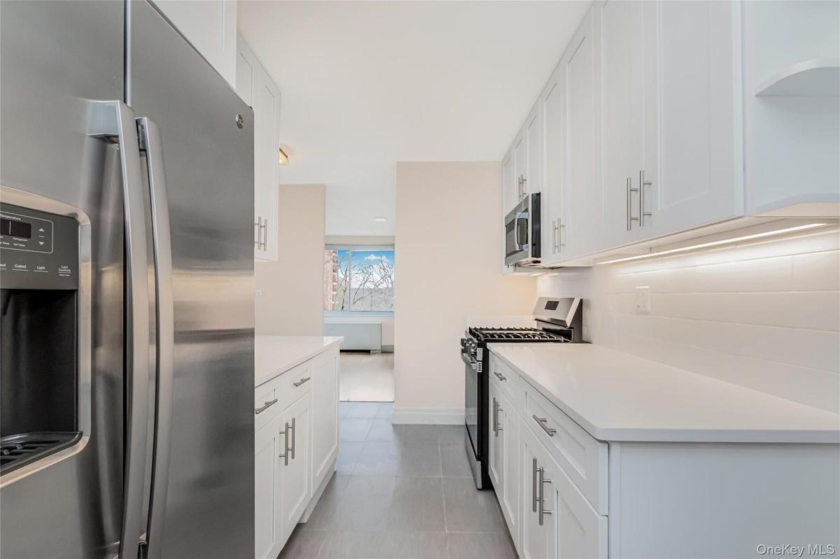 Kitchen with stainless steel appliances, white cabinetry, and light stone countertops