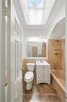 Full bathroom with vanity, tub / shower combination, tile walls, a skylight, and wainscoting