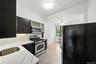 Kitchen featuring stainless steel appliances, dark cabinetry, decorative backsplash, light stone counters, and a ceiling fan