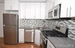 Kitchen with appliances with stainless steel finishes, white cabinetry, decorative backsplash, and dark wood-type flooring