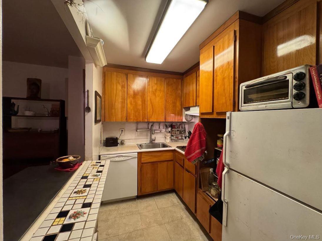 Kitchen featuring white appliances, brown cabinetry, tile countertops, and light tile patterned floors