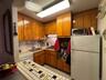 Kitchen featuring brown cabinets, white appliances, under cabinet range hood, backsplash, and tile countertops