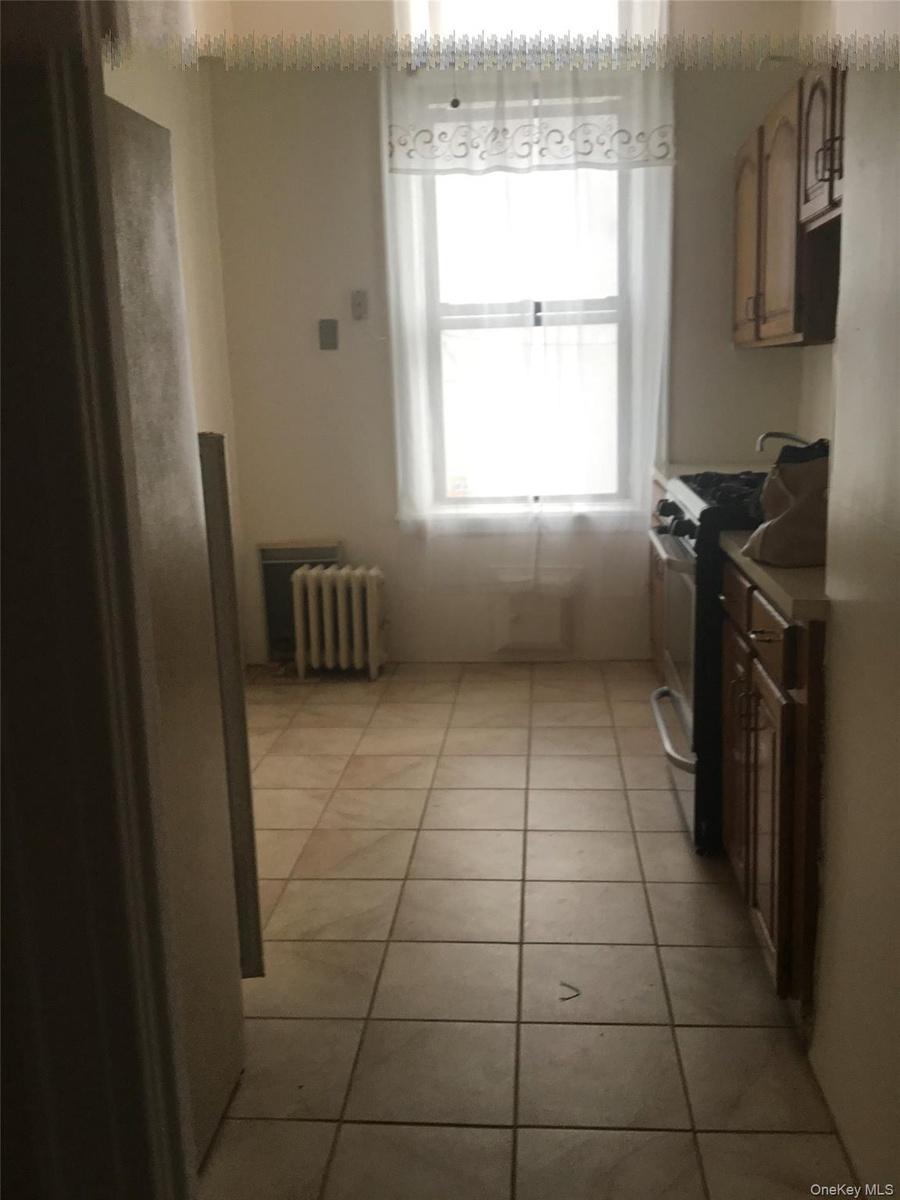 Kitchen featuring radiator, light tile patterned flooring, brown cabinets, and gas range