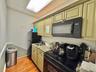 Kitchen featuring black appliances, cream cabinets, light wood-style flooring, light stone counters, and a paneled ceiling