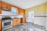 Kitchen featuring stainless steel gas range, under cabinet range hood, brown cabinets, light stone countertops, and a wainscoted wall