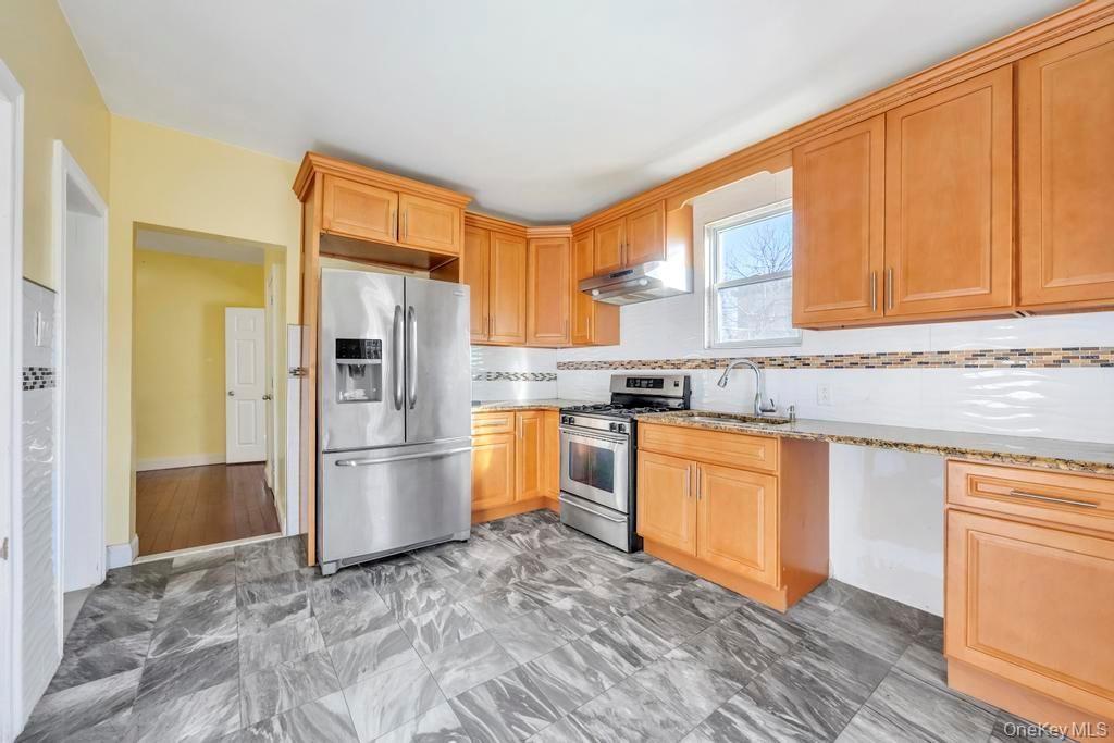 Kitchen with stainless steel appliances, light stone countertops, under cabinet range hood, decorative backsplash, and a heating unit