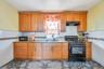 Kitchen with black appliances, brown cabinets, light stone counters, and under cabinet range hood